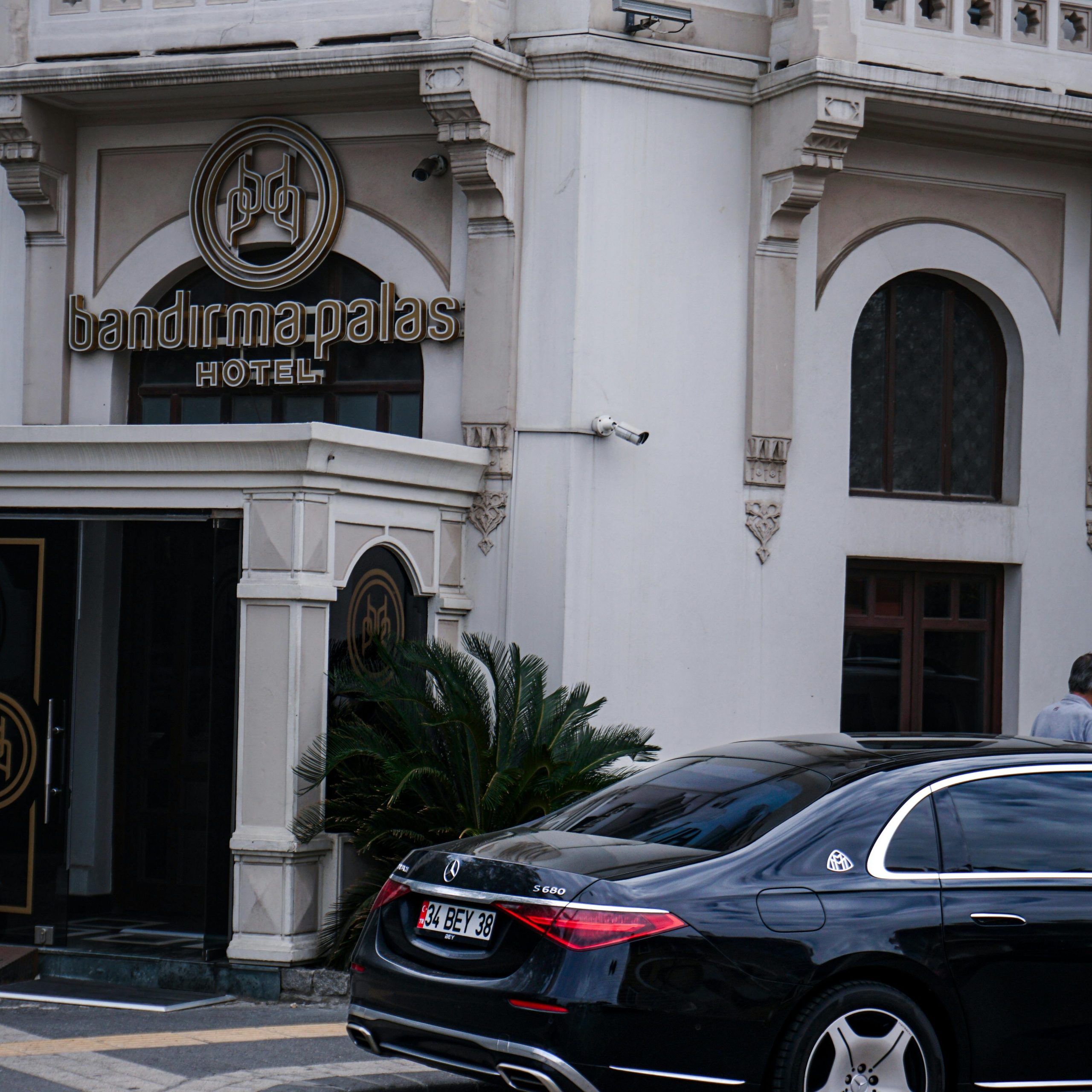 A luxury car parked in front of the historic Bandırma Palas Hotel, Turkey, showcasing urban architecture.